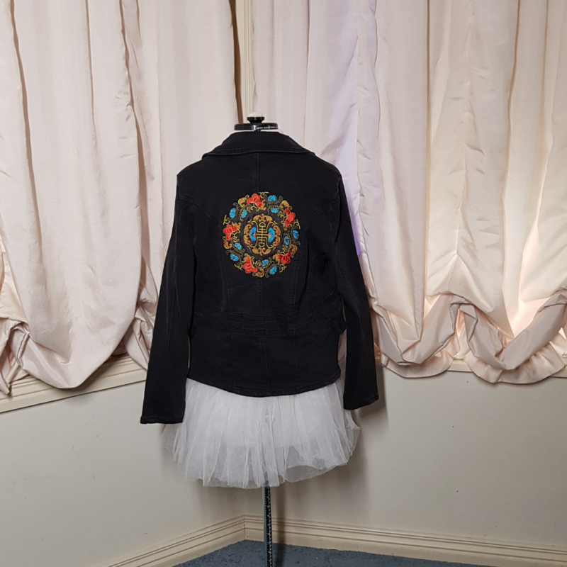 A Chinese Mandala Upcycled Denim Jacket displayed on a mannequin in front of a curtain.