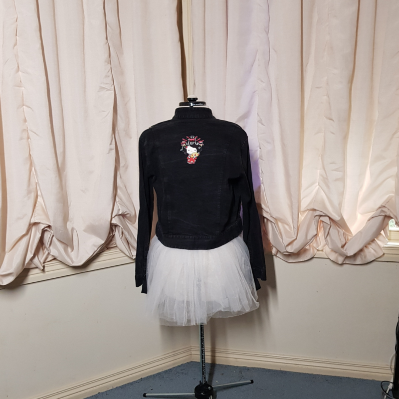 A mannequin wearing a Japanese Doll Upcycled Denim Jacket and tutu, showcased in front of a curtain.